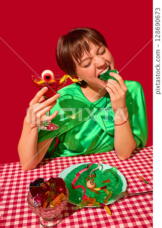 Woman aggressively eating jelly and holding cocktail with eyeball and candy worms Woman aggressively eating jelly and holding cocktail with eyeball and candy worms 128690673