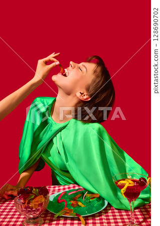 Woman laughing while being fed gummy candy by hand at surreal party table 128690702