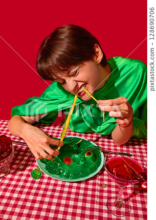 Aggressive woman biting long gummy snake from green jelly in intense playful scene 128690706