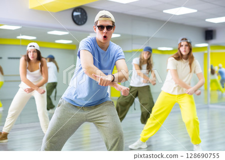 Active talented performing dance elements during lesson in modern fitness studio with mirrors Active talented performing dance elements during lesson in modern fitness studio with mirrors 128690755