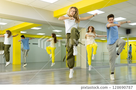 Teenagers dancing hip-hop in studio, learn dance moves together, wearing stylish outfit Teenagers dancing hip-hop in studio, learn dance moves together, wearing stylish outfit 128690787