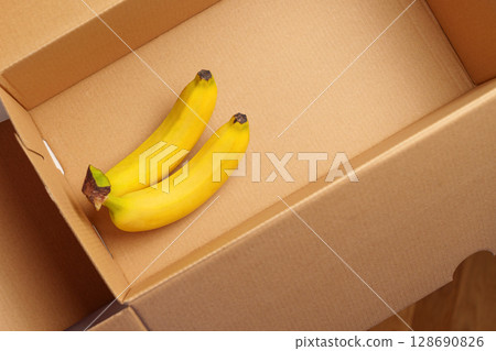 Bunch of ripe tropical bananas in cardboard box. Fruit packaging. Top view Bunch of ripe tropical bananas in cardboard box. Fruit packaging. Top view 128690826