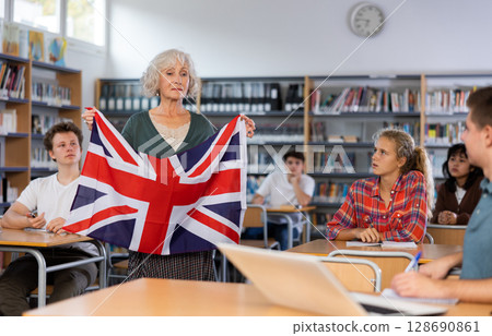 Mature female teacher shows scholchildren the national flag of Great Britain 128690861