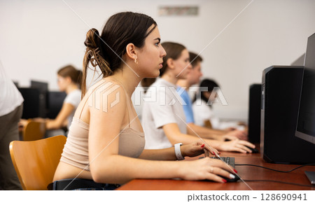 Teenage girl learning to use personal computer during lesson 128690941