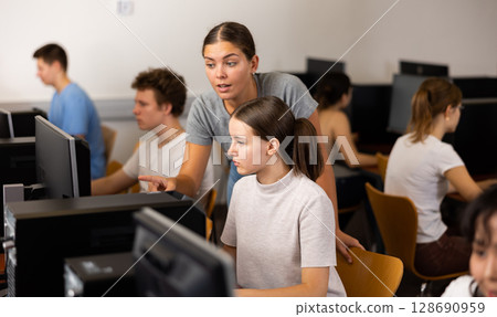 Young experienced female teacher helping girl pupil working with computer in college 128690959