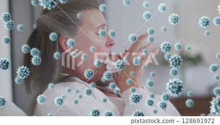 Sneezing mature woman holding crumpled tissue in softly lit home, with floating virus particles 128691972