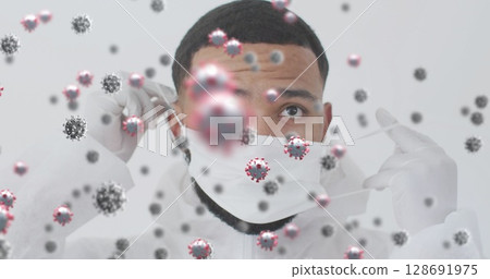 Adjusting man in protective suit and gloves fixing mask straps in studio, with virus particles 128691975