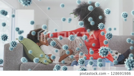 Checking caring mother feeling boy's forehead on sofa in modern living room, with virus graphics 128691986