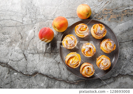 Peach roses mini tarts muffins made of puff pastry with powdered sugar close-up on a plate. horizontal top view Peach roses mini tarts muffins made of puff pastry with powdered sugar close-up on a plate. horizontal top view 128693008