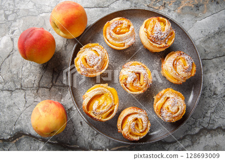 Fresh puff pastry peach mini tarts muffins close-up on plate. horizontal top view 128693009