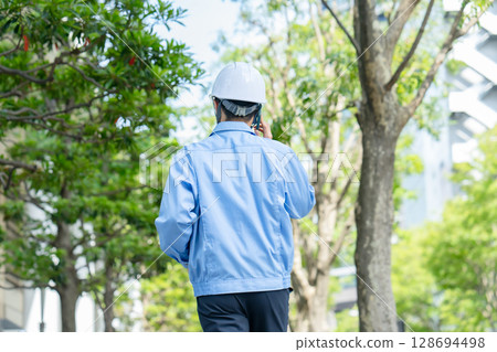 Middle-aged man in work clothes walking with smartphone, back view 128694498