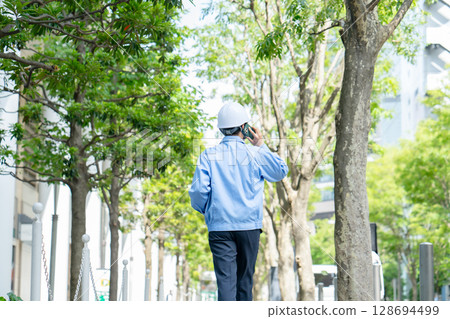 Middle-aged man in work clothes walking with smartphone, back view 128694499