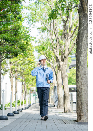 身穿工作服的中年男子拿著智慧型手機走路 身穿工作服的中年男子拿著智慧型手機走路 128694508