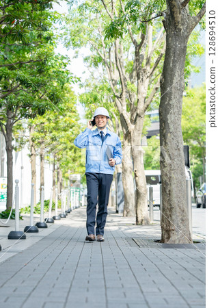 身穿工作服的中年男子拿著智慧型手機走路 128694510