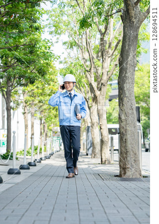 身穿工作服的中年男子拿著智慧型手機走路 128694511