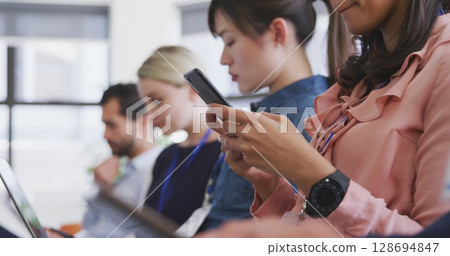 Scrolling woman in pink blouse holding smartphone in conference room, with smartwatch, copy space 128694847