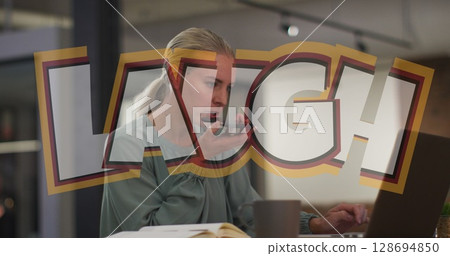 Holding smartphone, mid-adult woman speaking into phone in office, with laptop notebook coffee mug 128694850