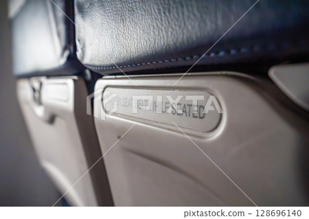 Close-up of seat sign on an airplane reading Fasten seat belt while seated. Air travel routine, safety instruction, and transportation awareness 128696140