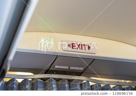 Airplane interior signage showing exit and lavatory icons. Flight safety, directions, and passenger information during air travel. 128696156