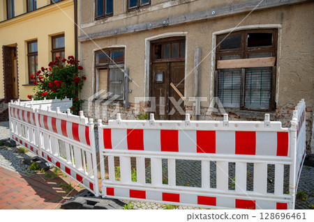 old building under renovation with red and white construction barriers and boarded window in Germany 128696461
