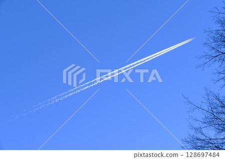 Scenery from an airplane window with a contrail flying in the blue sky 128697484