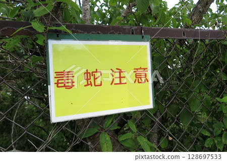 A "Beware of poisonous snakes" sign attached to a fence in a mountainous area 128697533