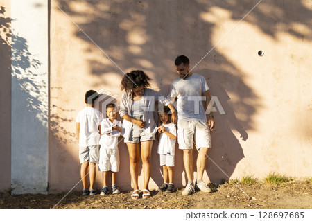 Happy family posing together against a wall on a sunny day 128697685