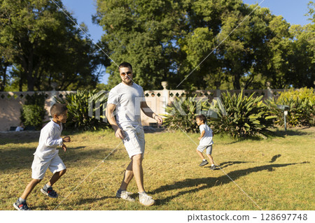 Father playing with sons in park on sunny day 128697748