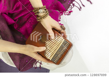 Woman holding kalimba in her hands and playing. Concept of Relaxing at home, Me time and self care and sound meditation. Woman enjoy the melodious sound of the thumb piano playing. Closeup Woman holding kalimba in her hands and playing. Concept of Relaxing at home, Me time and self care and sound meditation. Woman enjoy the melodious sound of the thumb piano playing. Closeup 128697899