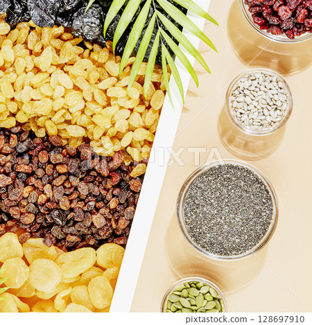 Dry fruits, nuts and seeds assortment on beige background with palm leaves. Healthy snack - mix of organic nuts and dry fruits. Vegan and vegetarian products. Healthy food. Flat lay 128697910