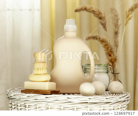 Natural laundry detergent mockup. Washing detergent concept with bottle of washing gel or fabric softener on a white laundry basket with natural soap, brush and laundry balls. Laundry day. Front view 128697917