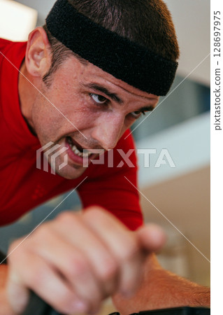 A triathlete riding a triathlon bike on a machine simulation in a modern living room. Training during pandemic conditions. A triathlete riding a triathlon bike on a machine simulation in a modern living room. Training during pandemic conditions. 128697975