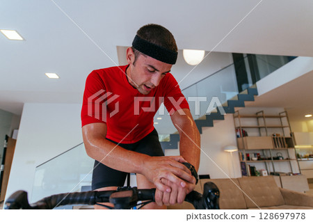 A triathlete riding a triathlon bike on a machine simulation in a modern living room. Training during pandemic conditions. 128697978