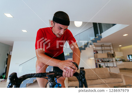 A triathlete riding a triathlon bike on a machine simulation in a modern living room. Training during pandemic conditions. A triathlete riding a triathlon bike on a machine simulation in a modern living room. Training during pandemic conditions. 128697979