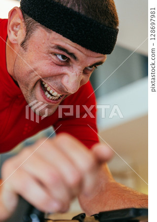 A triathlete riding a triathlon bike on a machine simulation in a modern living room. Training during pandemic conditions. 128697981