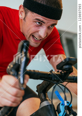 A triathlete riding a triathlon bike on a machine simulation in a modern living room. Training during pandemic conditions. 128697993
