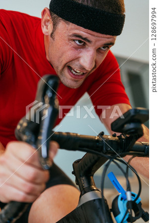 A triathlete riding a triathlon bike on a machine simulation in a modern living room. Training during pandemic conditions. 128697994