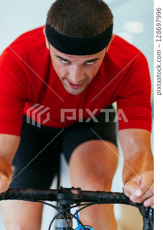 A triathlete riding a triathlon bike on a machine simulation in a modern living room. Training during pandemic conditions. A triathlete riding a triathlon bike on a machine simulation in a modern living room. Training during pandemic conditions. 128697996