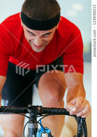 A triathlete riding a triathlon bike on a machine simulation in a modern living room. Training during pandemic conditions. 128698015