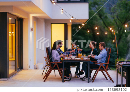A group of young diverse people having dinner on the terrace of a modern house in the evening. Fun for friends and family. Celebration of holidays, weddings with barbecue 128698102