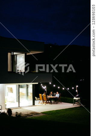 A group of young diverse people having dinner on the terrace of a modern house in the evening. Fun for friends and family. Celebration of holidays, weddings with barbecue 128698103