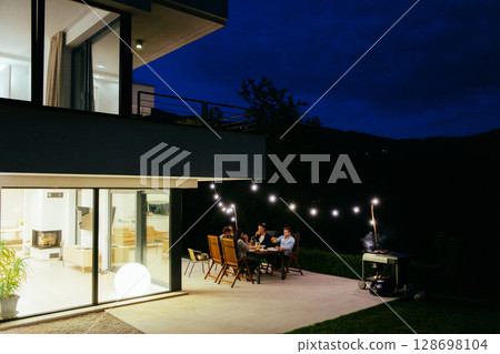 A group of young diverse people having dinner on the terrace of a modern house in the evening. Fun for friends and family. Celebration of holidays, weddings with barbecue 128698104