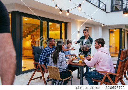 A group of young diverse people having dinner on the terrace of a modern house in the evening. Fun for friends and family. Celebration of holidays, weddings with barbecue 128698121