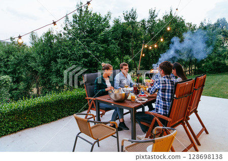 A group of young diverse people having dinner on the terrace of a modern house in the evening. Fun for friends and family. Celebration of holidays, weddings with barbecue 128698138