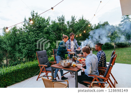 A group of young diverse people having dinner on the terrace of a modern house in the evening. Fun for friends and family. Celebration of holidays, weddings with barbecue 128698149