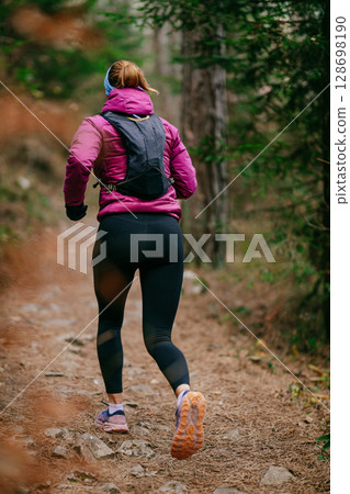 Determined Female Athlete Running with Focus Through a Dense Pine Forest, Embracing Strength and Nature Determined Female Athlete Running with Focus Through a Dense Pine Forest, Embracing Strength and Nature 128698190