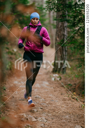 Determined Female Athlete Running with Focus Through a Dense Pine Forest, Embracing Strength and Nature 128698200