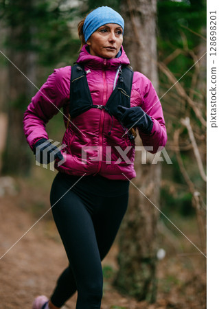 Determined Female Athlete Running with Focus Through a Dense Pine Forest, Embracing Strength and Nature Determined Female Athlete Running with Focus Through a Dense Pine Forest, Embracing Strength and Nature 128698201