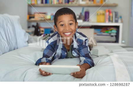 Smiling boy using tablet on bed at home, enjoying leisure time Smiling boy using tablet on bed at home, enjoying leisure time 128698287