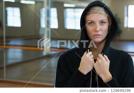 Confident woman in hoodie standing in dance studio, looking determined 128698296